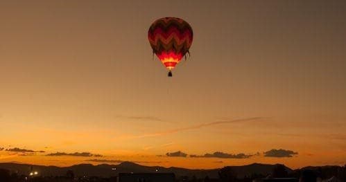 Single hot air balloon silhouetted at sunset over open landscape