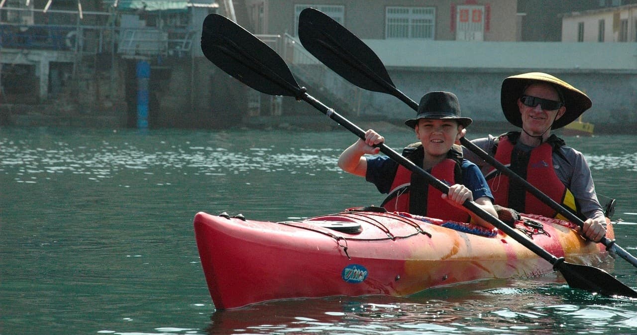 Two kayakers paddling a red tandem kayak in calm harbor waters