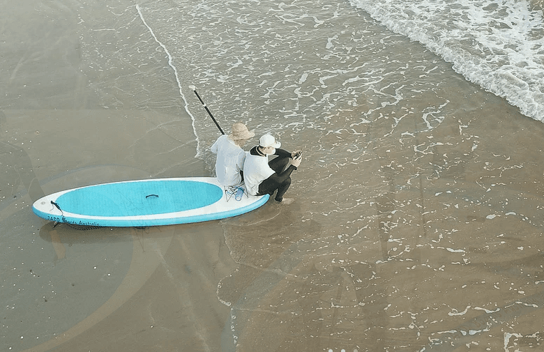 Aerial paddleboard in shallow turquoise bay near sandy beach