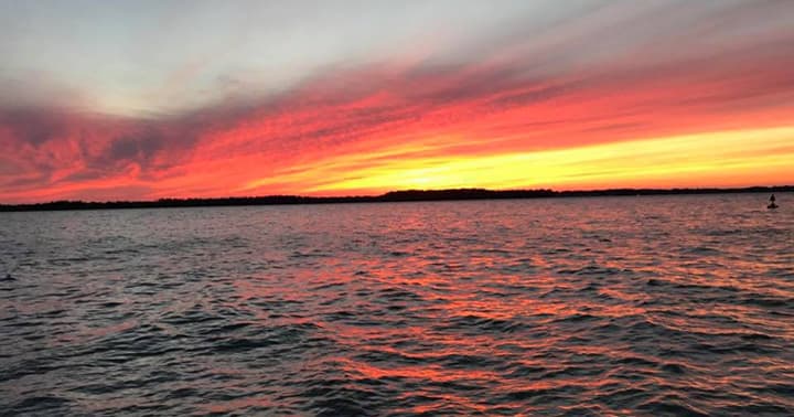 Sunset over open water with vibrant orange sky and horizon
