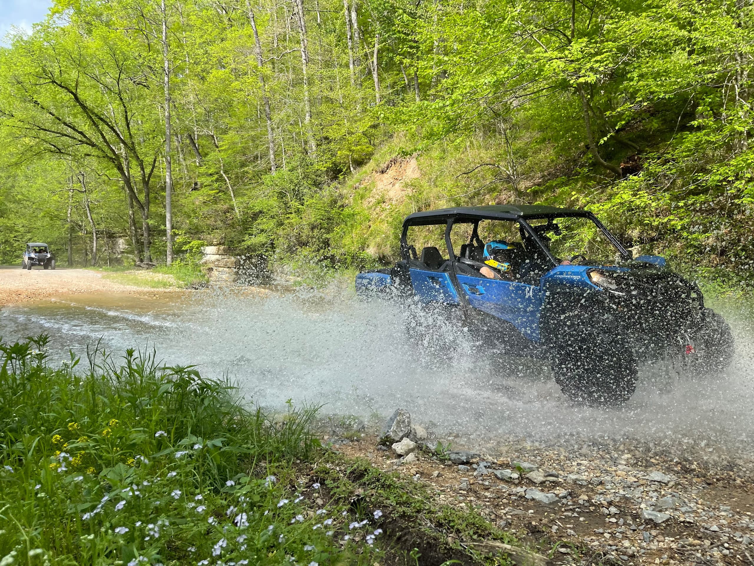 Side-by-side vehicle creating dramatic water spray crossing woodland stream