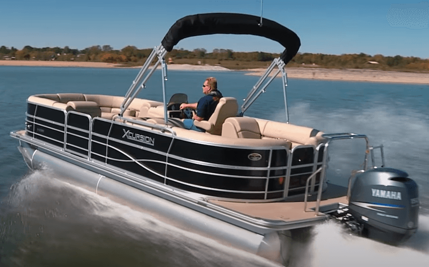 Wide-angle pontoon boat speeding on lake with wake and trees
