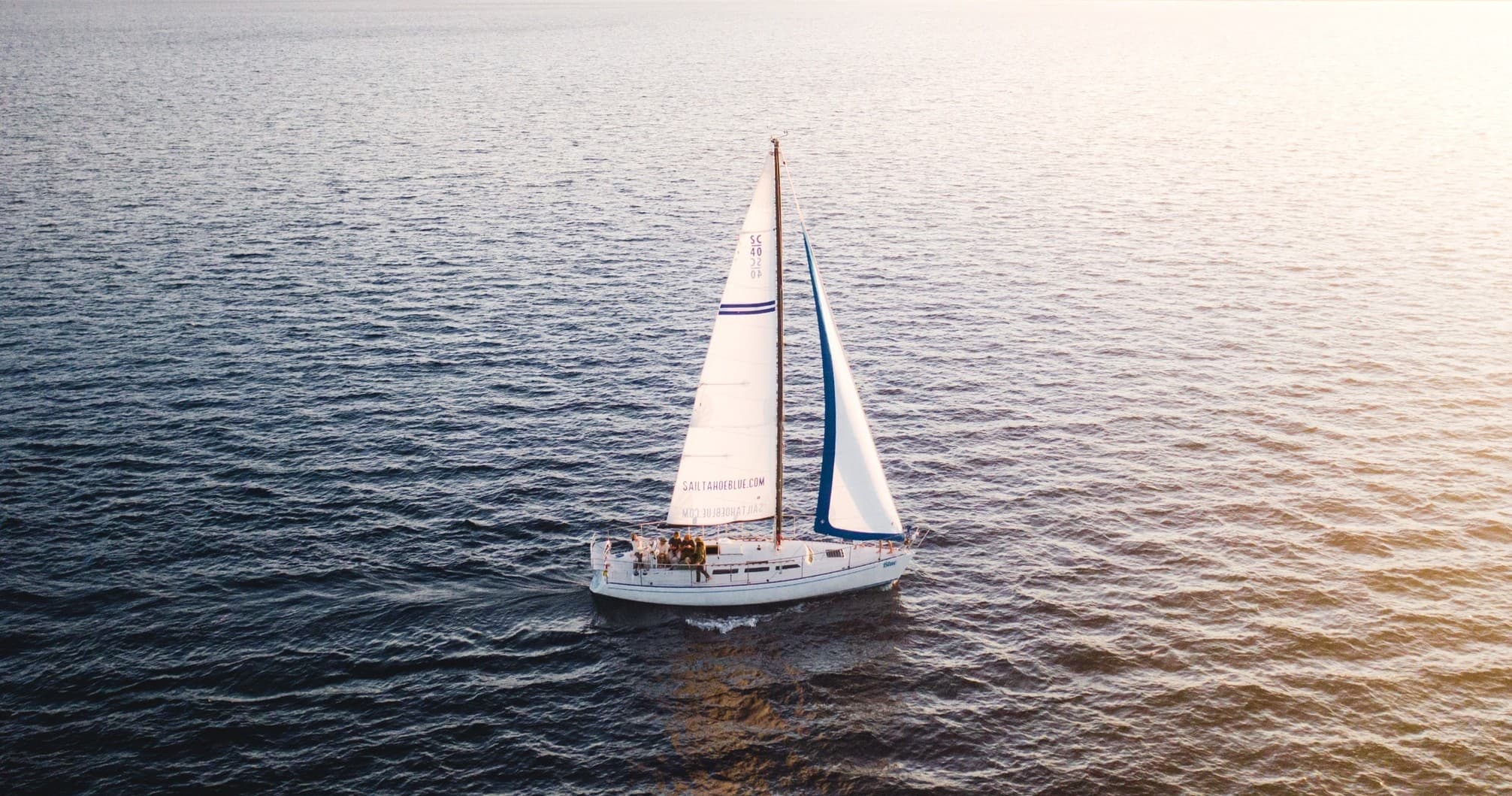 Aerial view of sailboat cruising calm open ocean at sunset