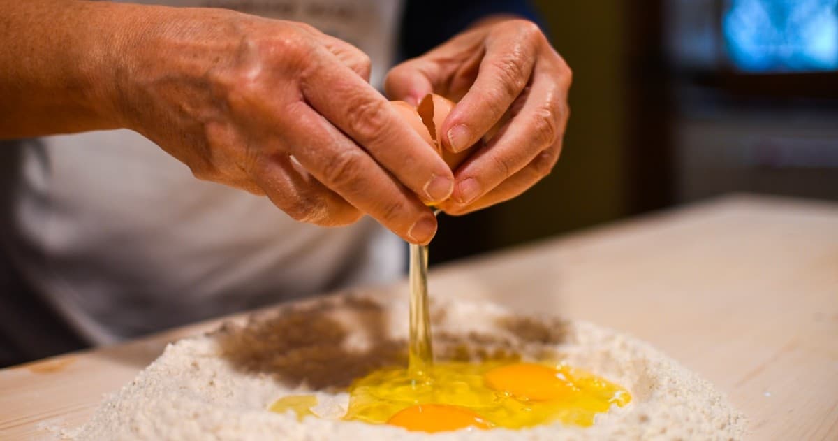 Chef cracking egg into flour mound preparing fresh pasta dough