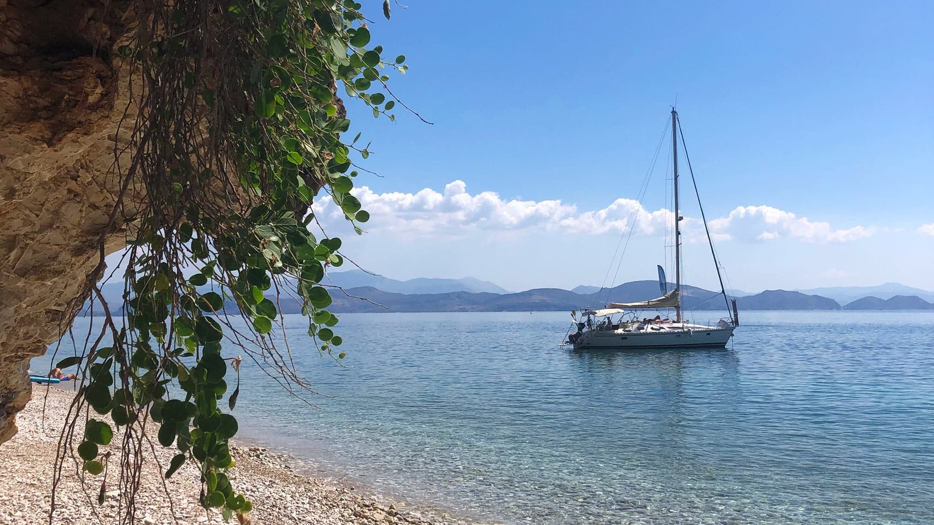 Sailboat moored by pebbled beach with overhanging vines, Nafplio bay