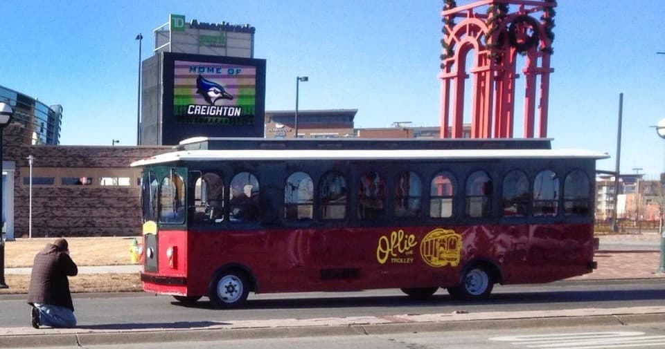 Red trolley driving in urban setting past billboards on city tour