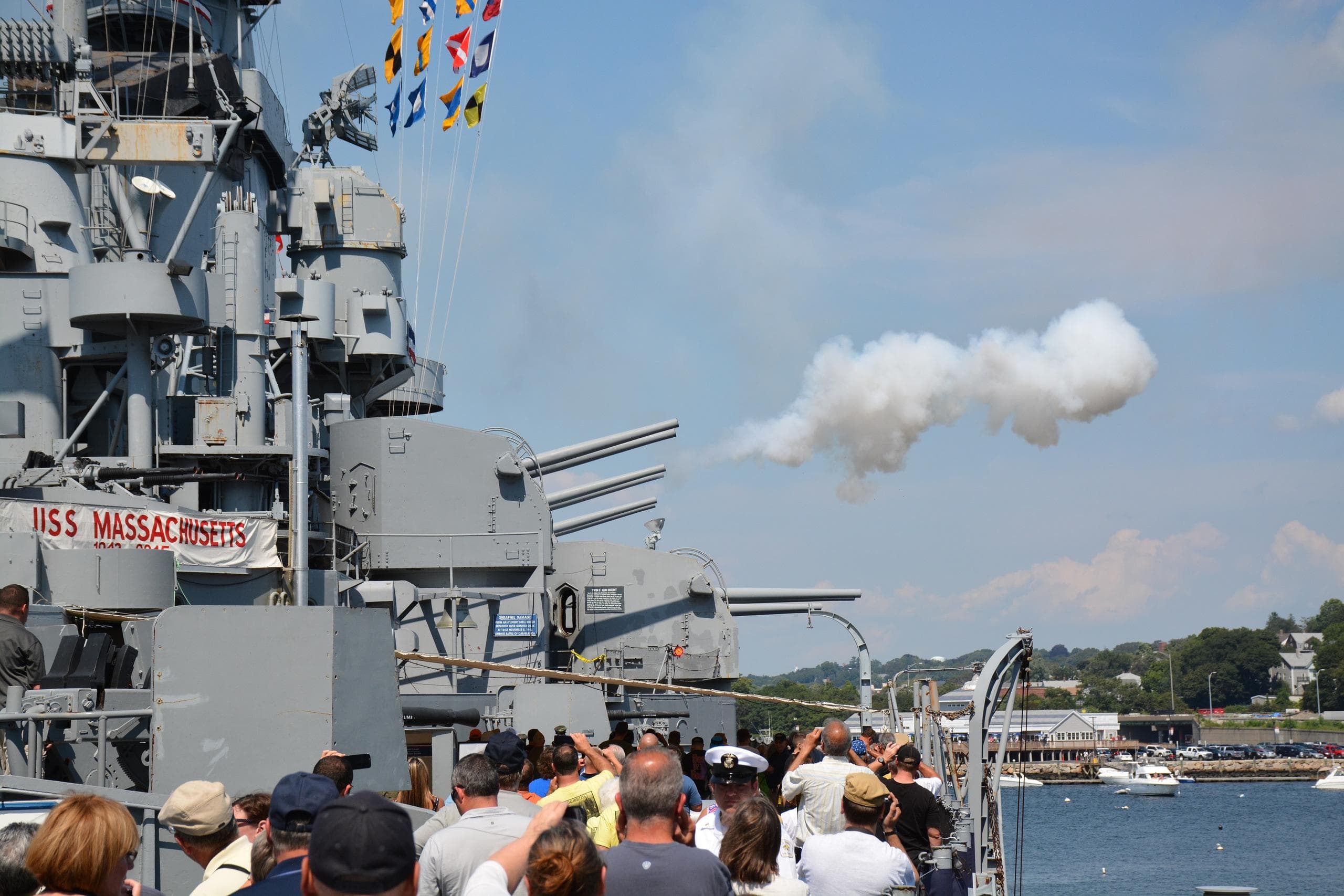 Crowd watching naval gun salute aboard historic battleship at pier