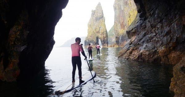 Paddleboarders navigating sea cave with rocky cliffs and arches