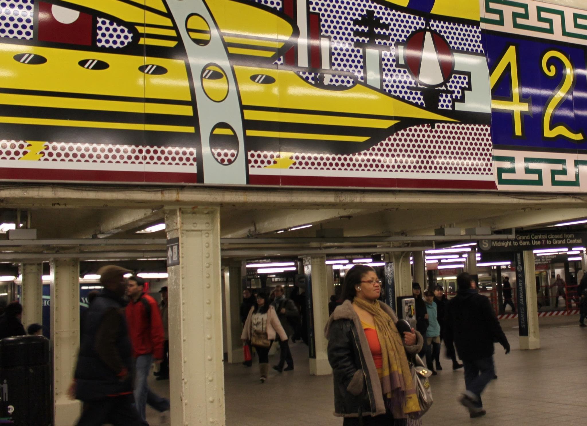 Commuters passing colorful mural in NYC subway station, urban tour
