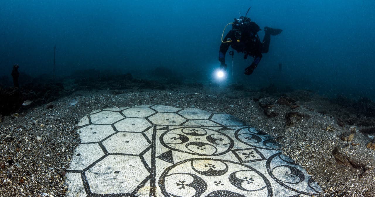 Scuba diver surveying tiled mosaic ruins on clear seabed