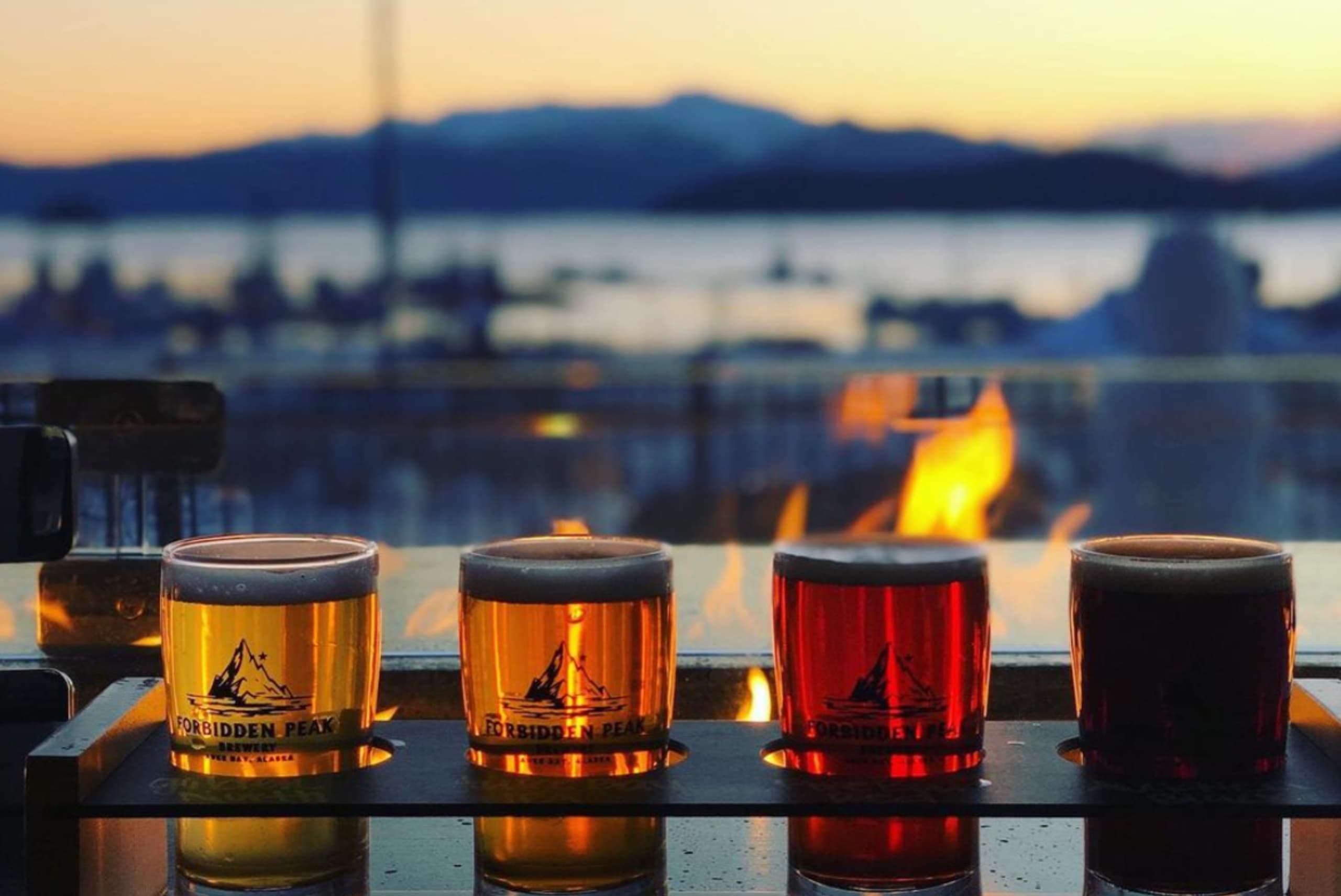 Beer tasting flight on waterfront patio with mountain sunset