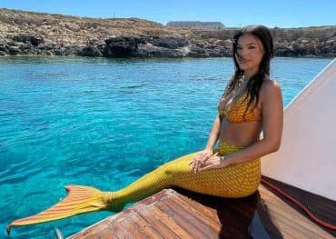 Woman in mermaid tail relaxing on boat over clear sea