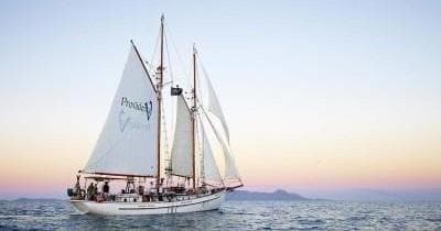 Classic schooner sailing at sunset across calm coastal sea