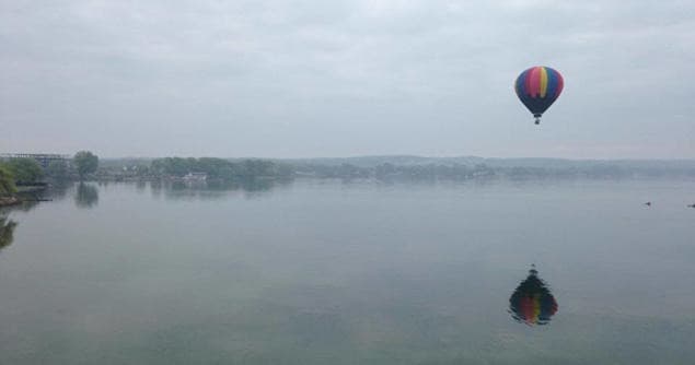 Hot air balloon floating over calm lake with reflection