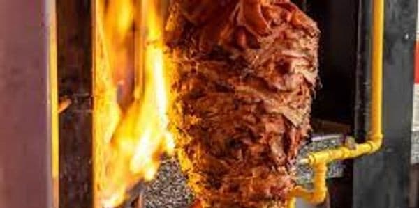 Rotating shawarma spit grilling over open flame at street vendor