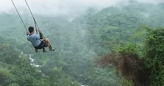 Person on swing over misty green mountain valley, jungle viewpoint