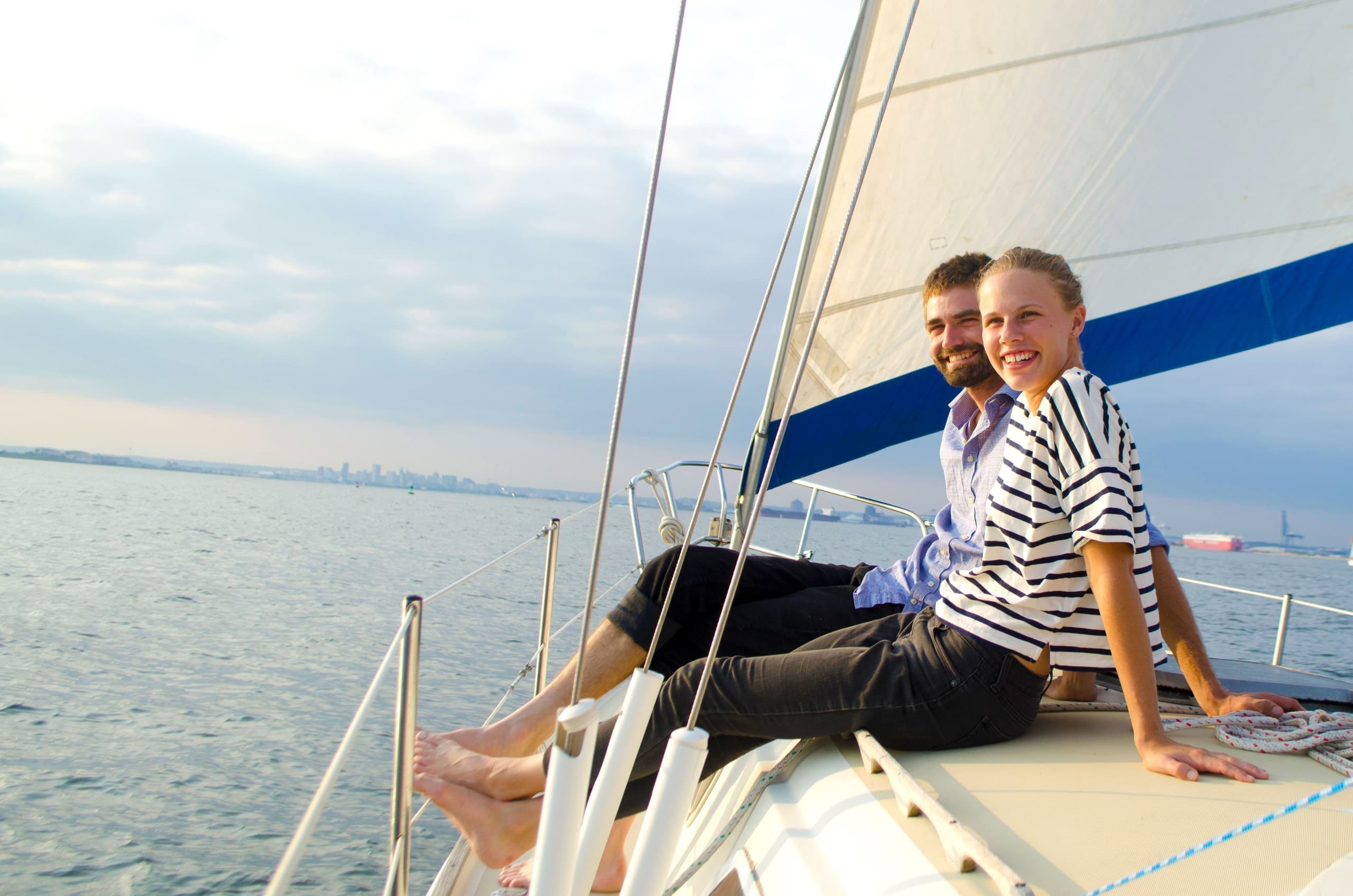 Couple relaxing on sailboat deck with city skyline on horizon