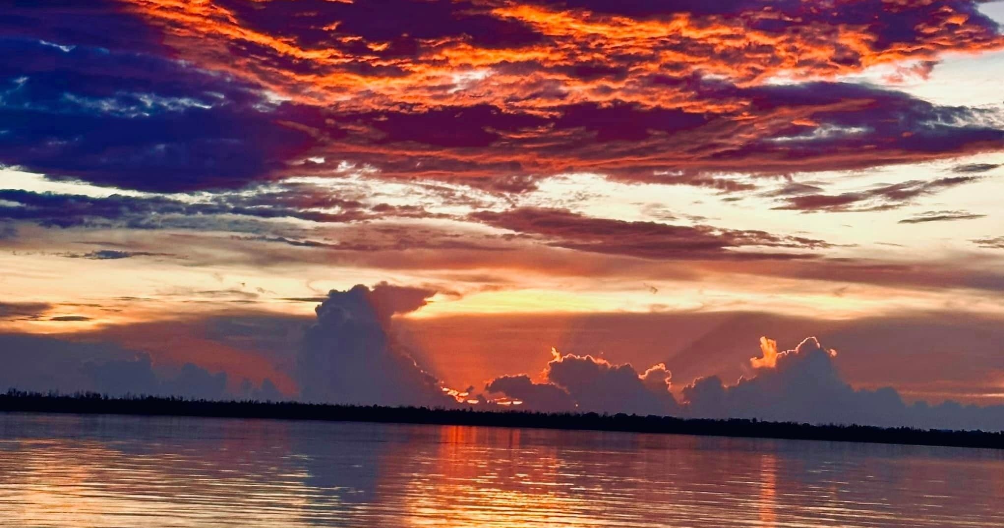 Vibrant coastal sunset over calm bay with dramatic clouds