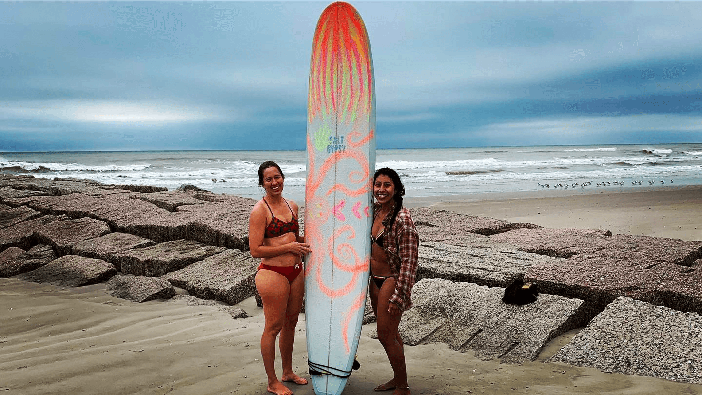 Two surfers posing on sandy beach beside colorful longboard