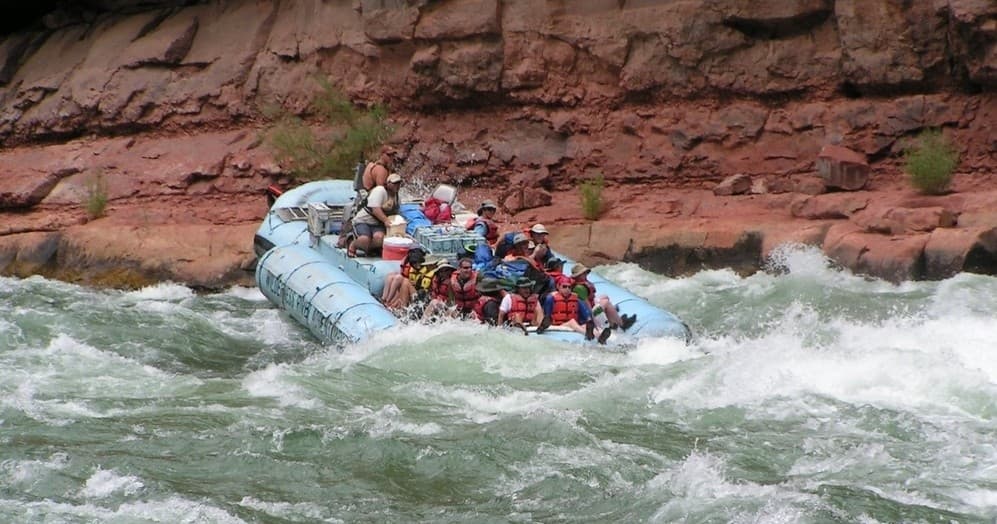 Group raft cutting through whitewater rapids with canyon backdrop