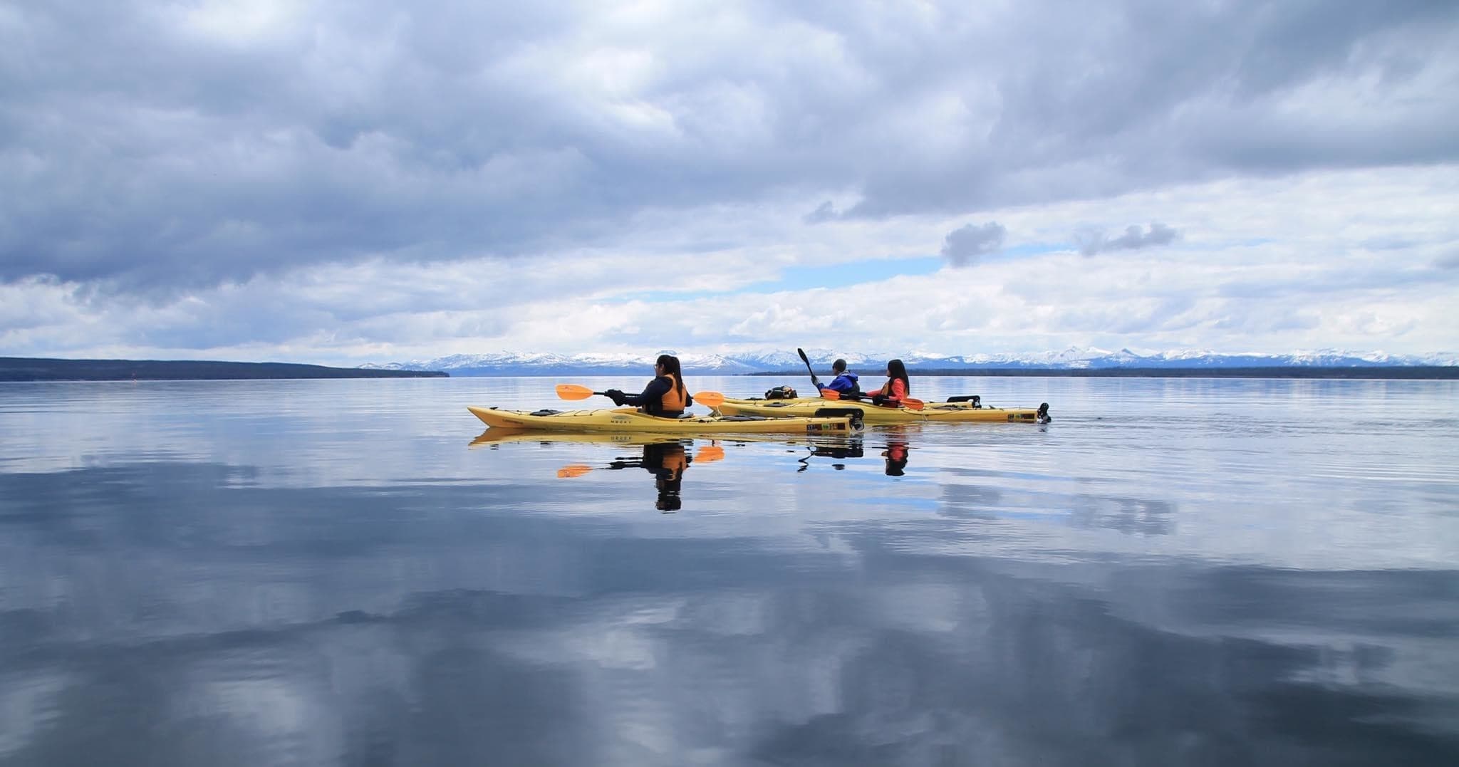 Group kayakers paddling across mirrored lake under dramatic sky