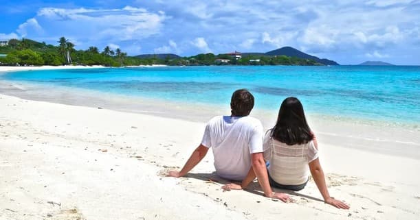 Couple sitting on white sand beach enjoying calm turquoise water