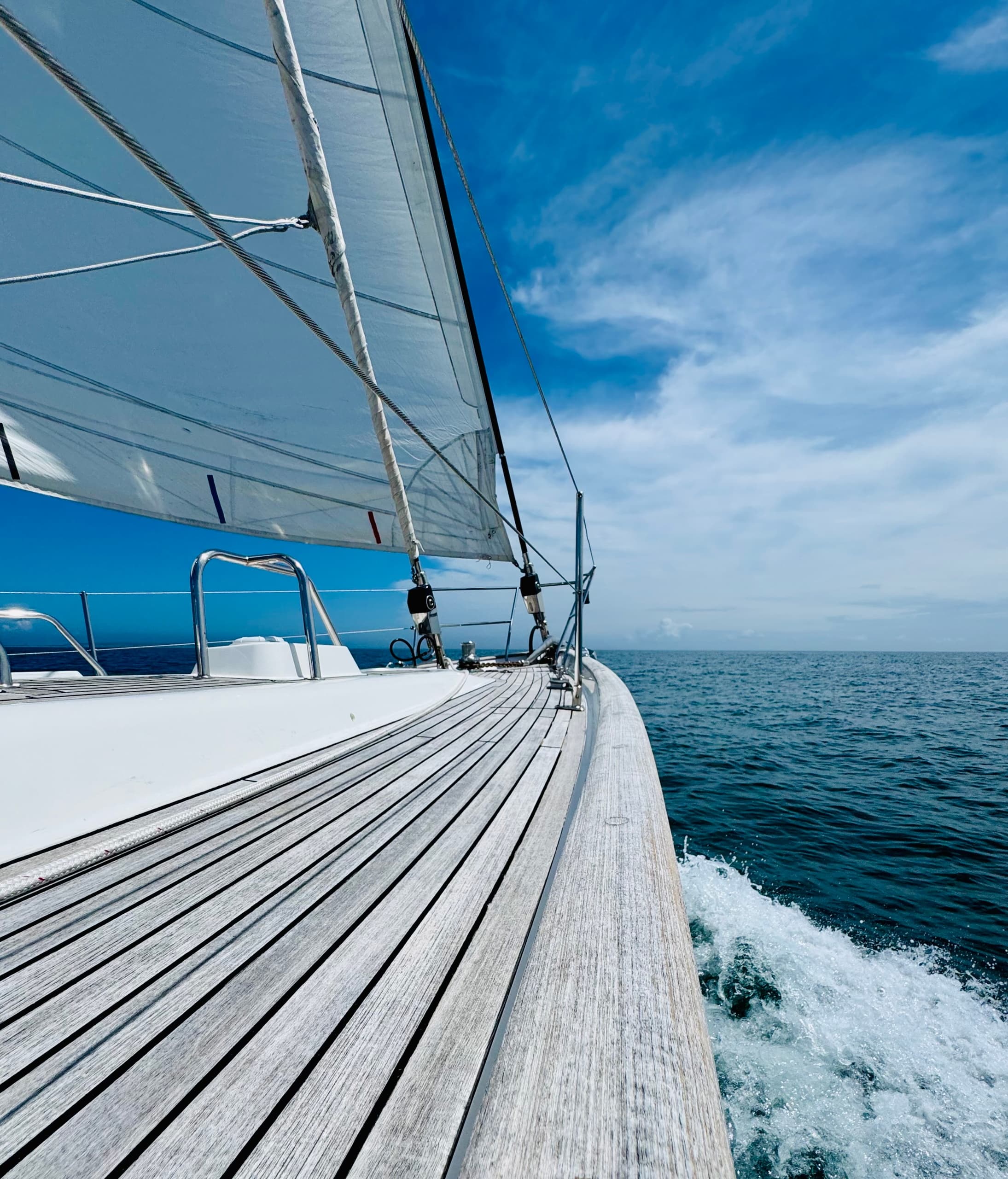 Sailboat cruising on open ocean, deck foreground and sails