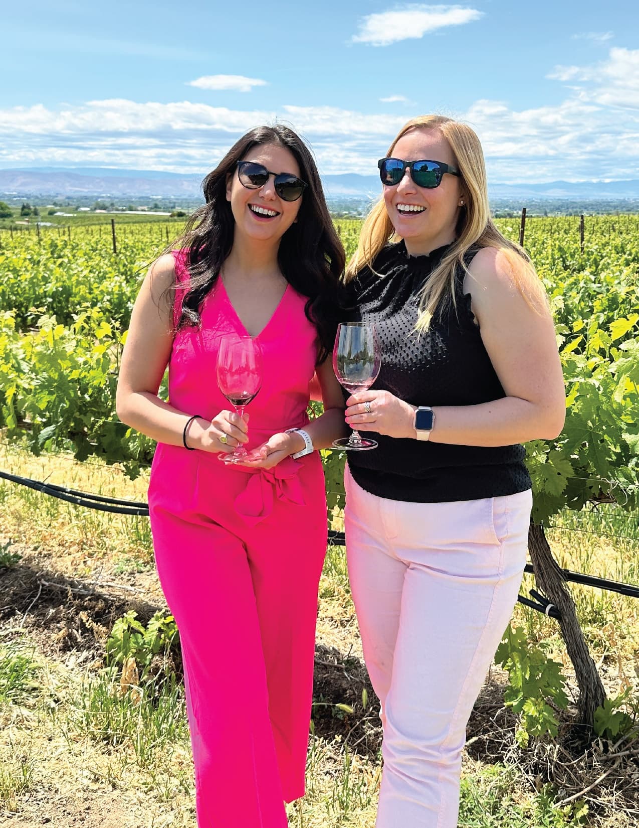 Two women tasting wine in vineyard with scenic hills