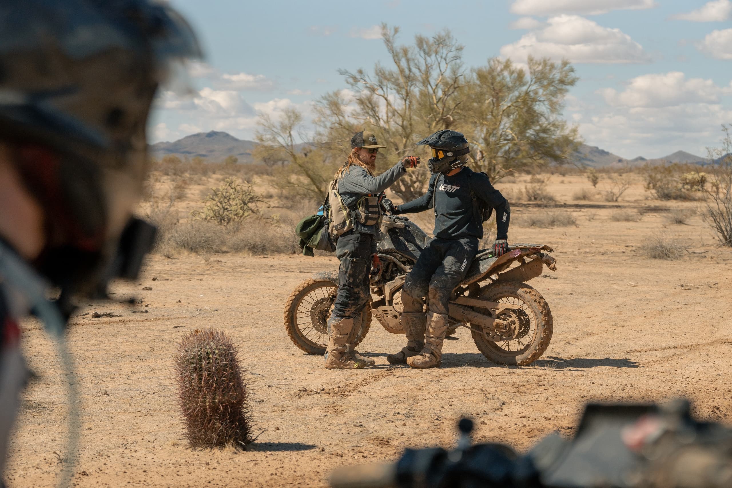 Two riders parked beside dirt trail with desert foreground blur