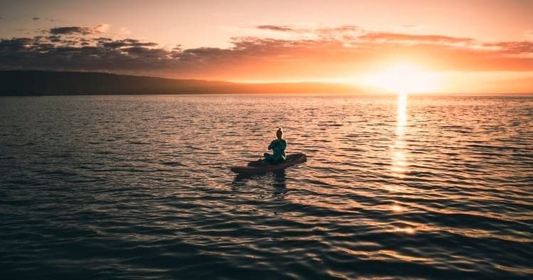 Kayaker paddling at sunset across calm open ocean near horizon