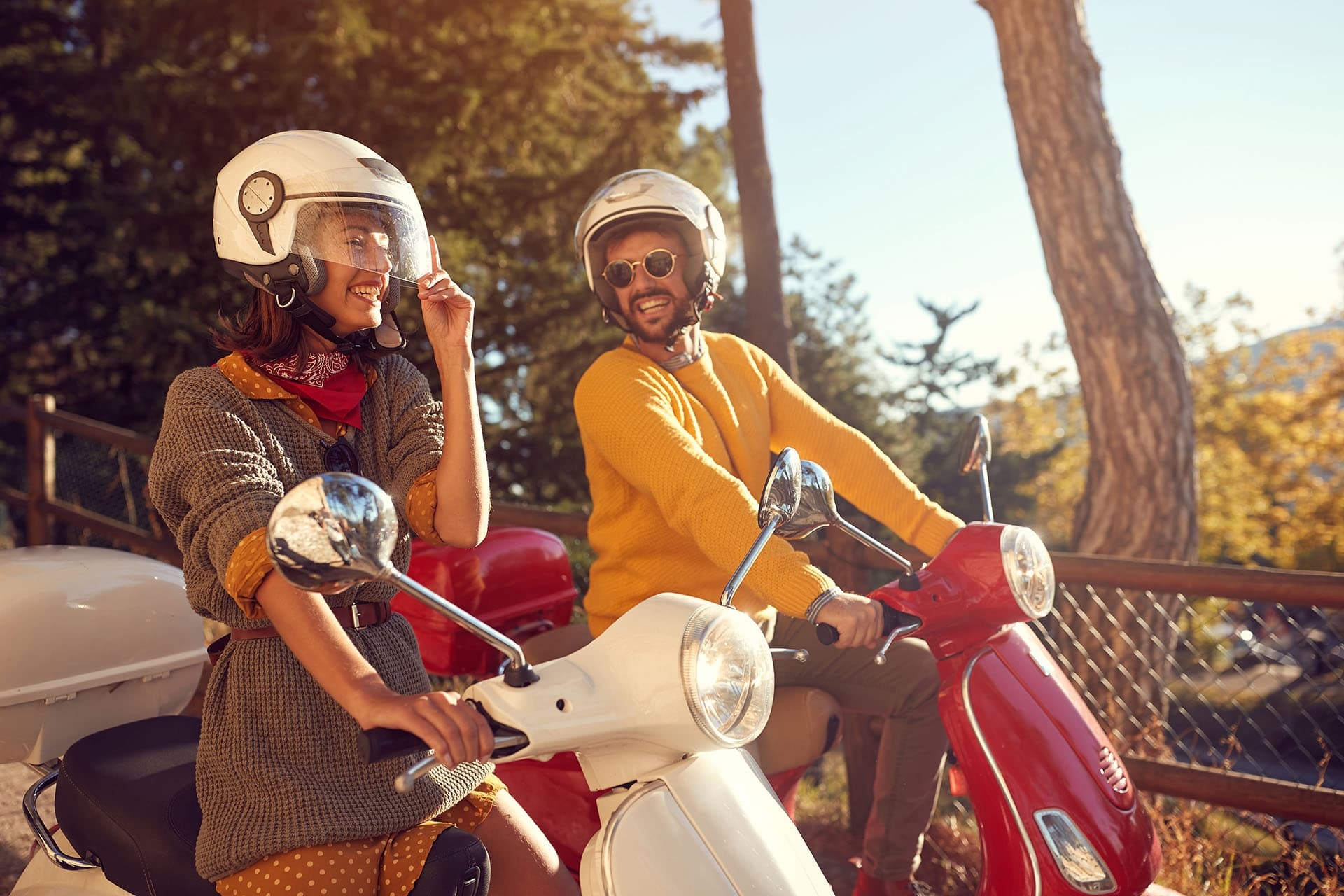 Smiling duo on vintage scooters in sunlit park road