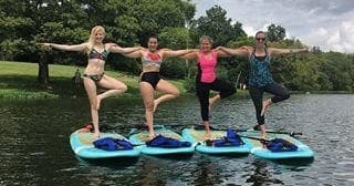 Four women practicing standup paddleboard yoga on calm lake