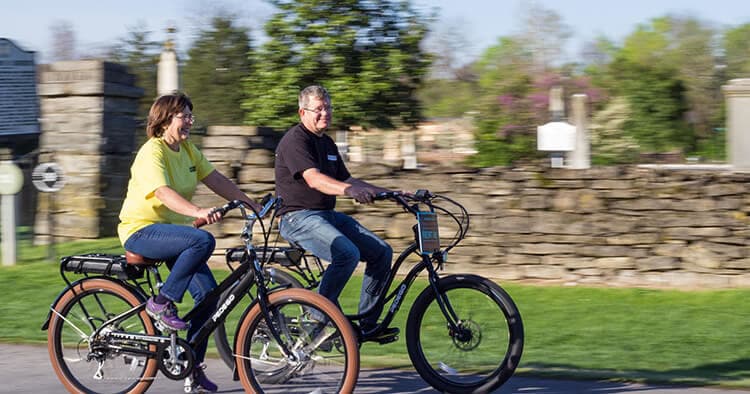 Couple biking on country road past stone wall and green fields