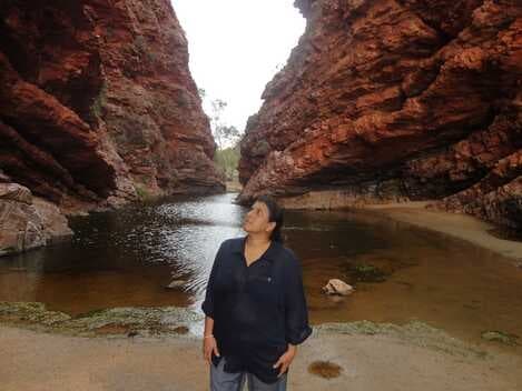 Traveler standing by water inside narrow red rock gorge