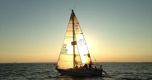 Sailboat silhouetted at sunset on tranquil open ocean sail