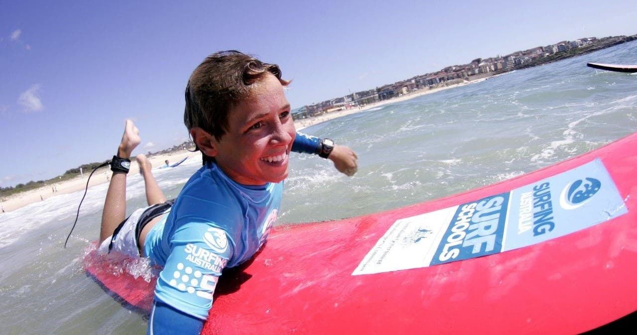 Young surfer lying on red surfboard in shallow ocean