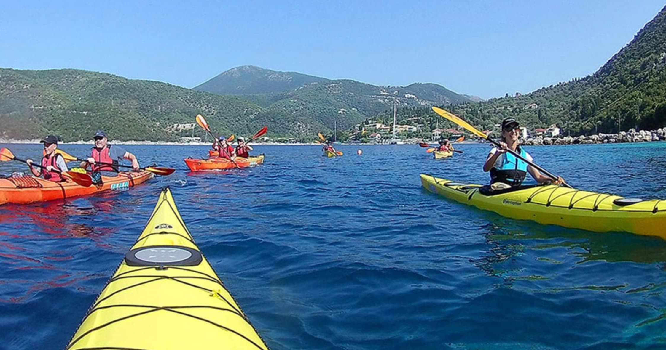 Kayak bow leading through blue sea toward coastal mountains