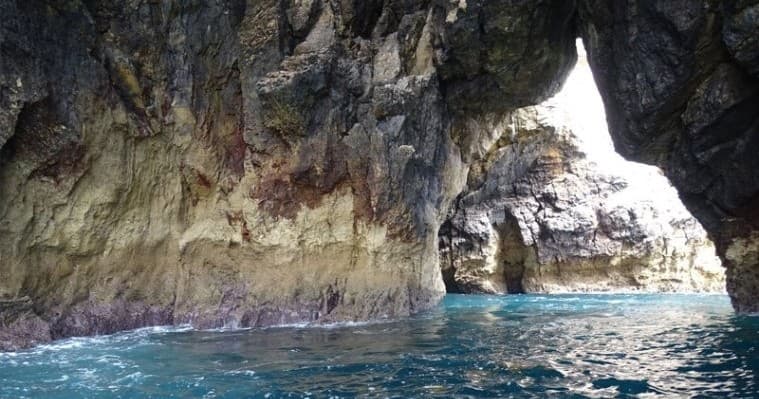 Boat entering sea cave and coastal rock arch, turquoise ocean view