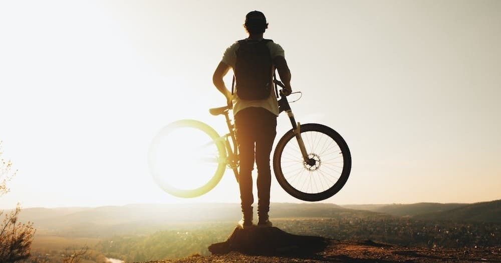 Mountain biker silhouetted on hill at sunset with wide valley view