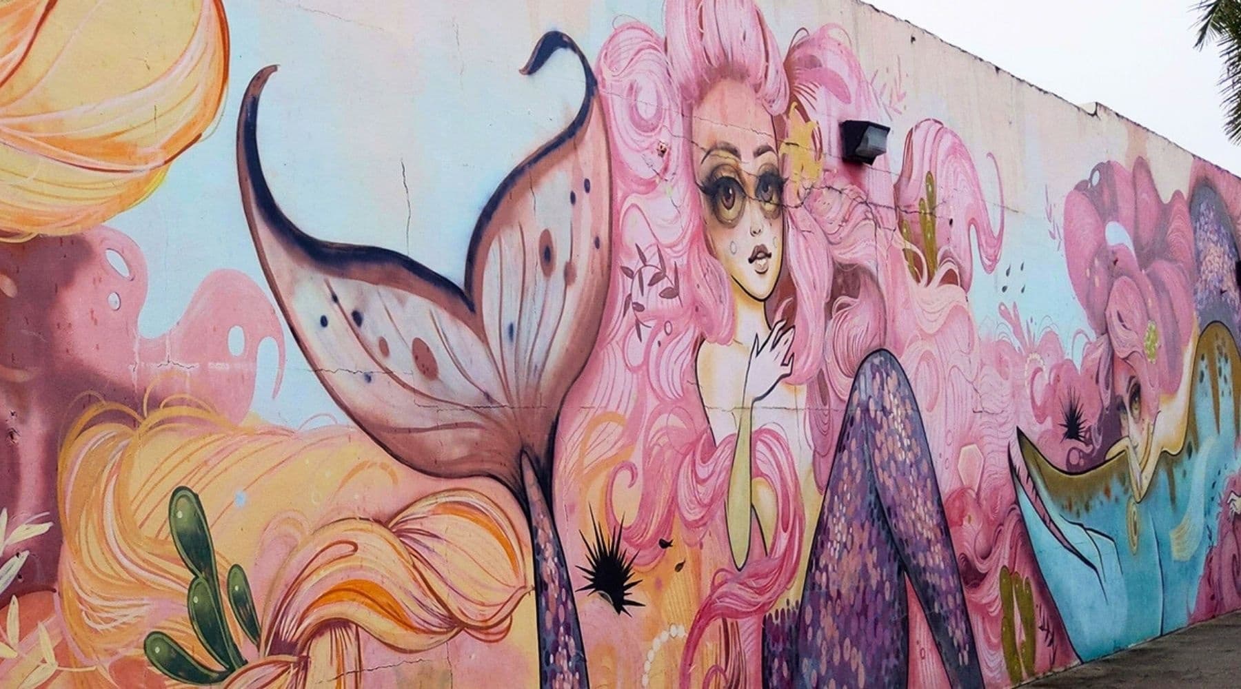 Vibrant mermaid street mural on exterior wall, beachside neighborhood