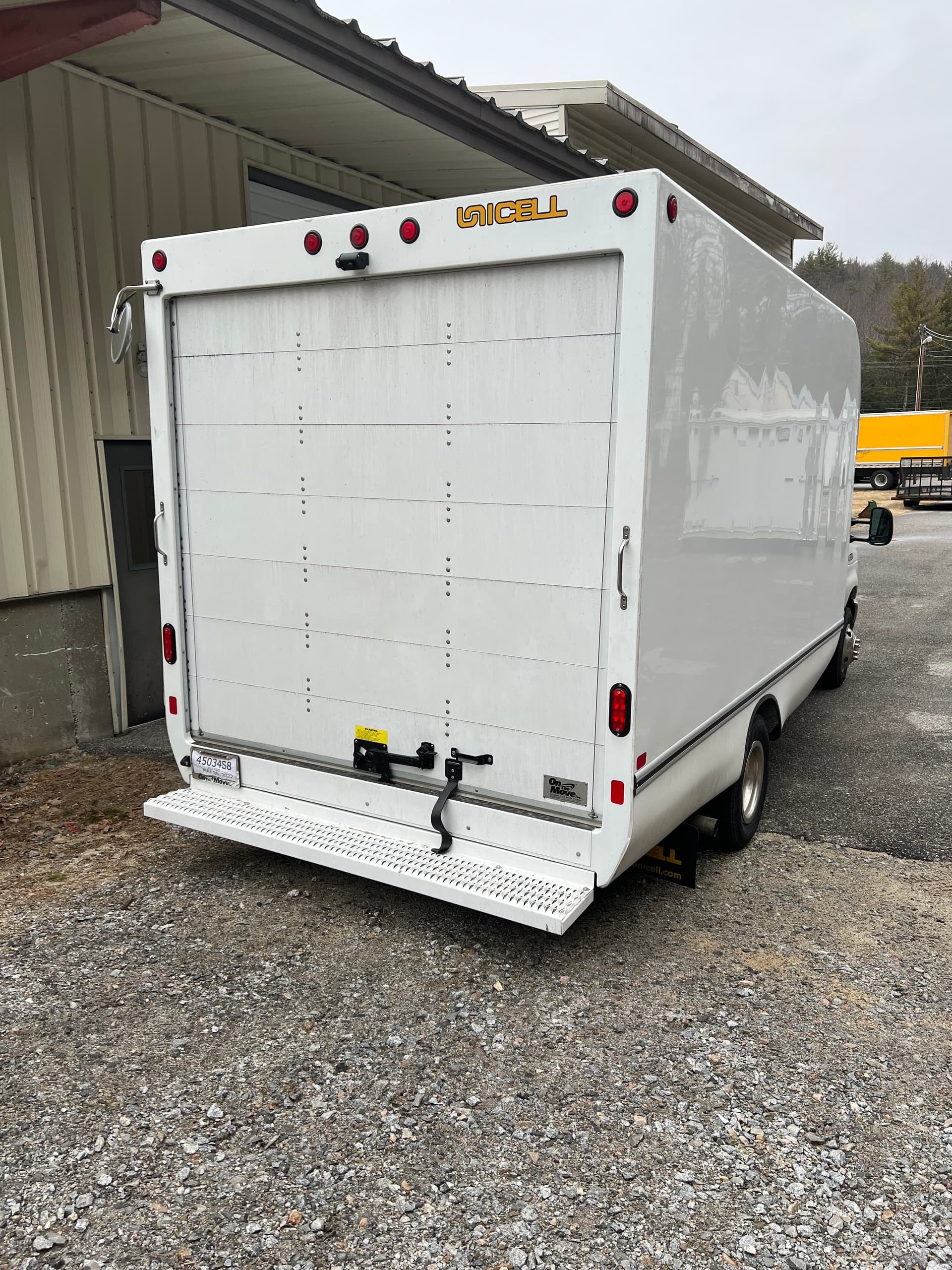 White box moving truck parked at warehouse gravel lot, ready for loading