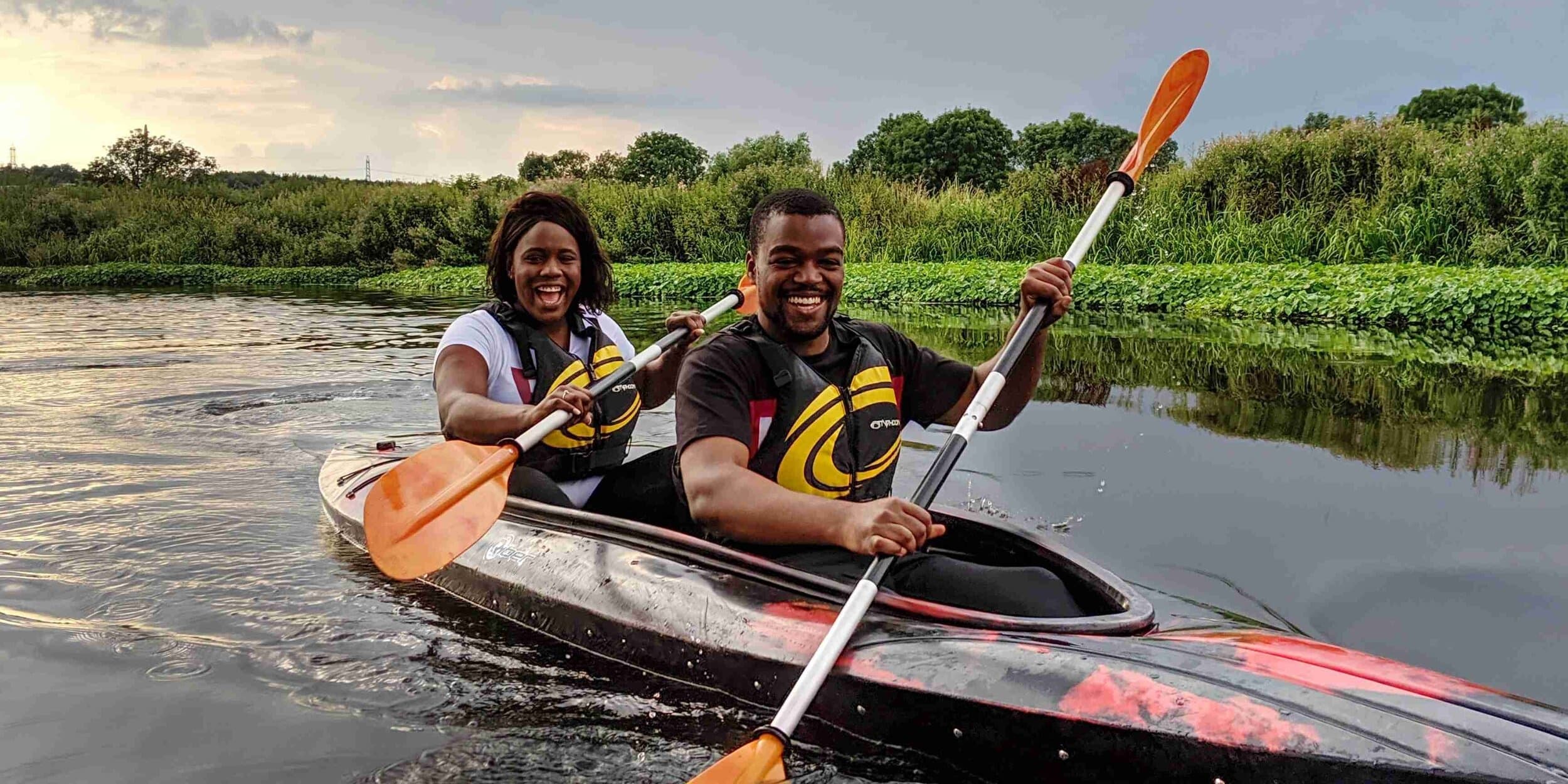 Couple kayaking at sunset through calm river landscape