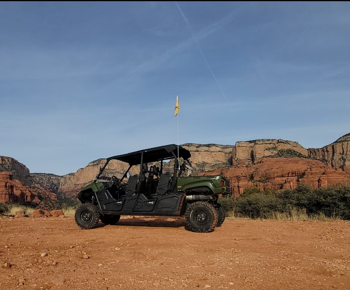 Extended multi-seat UTV on red sandstone trail beneath desert cliffs