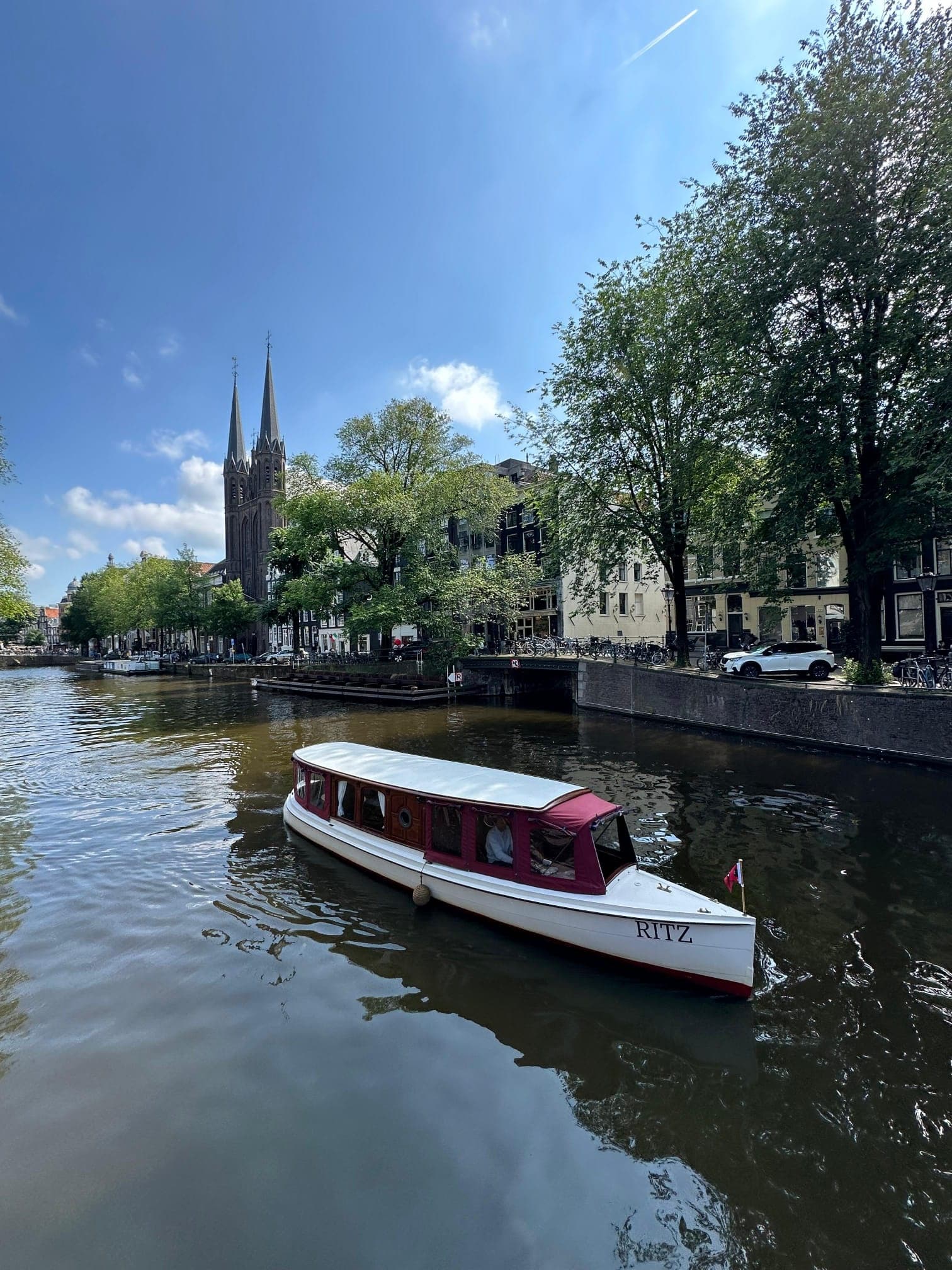 Small covered boat cruising near Amsterdam cathedral on canal