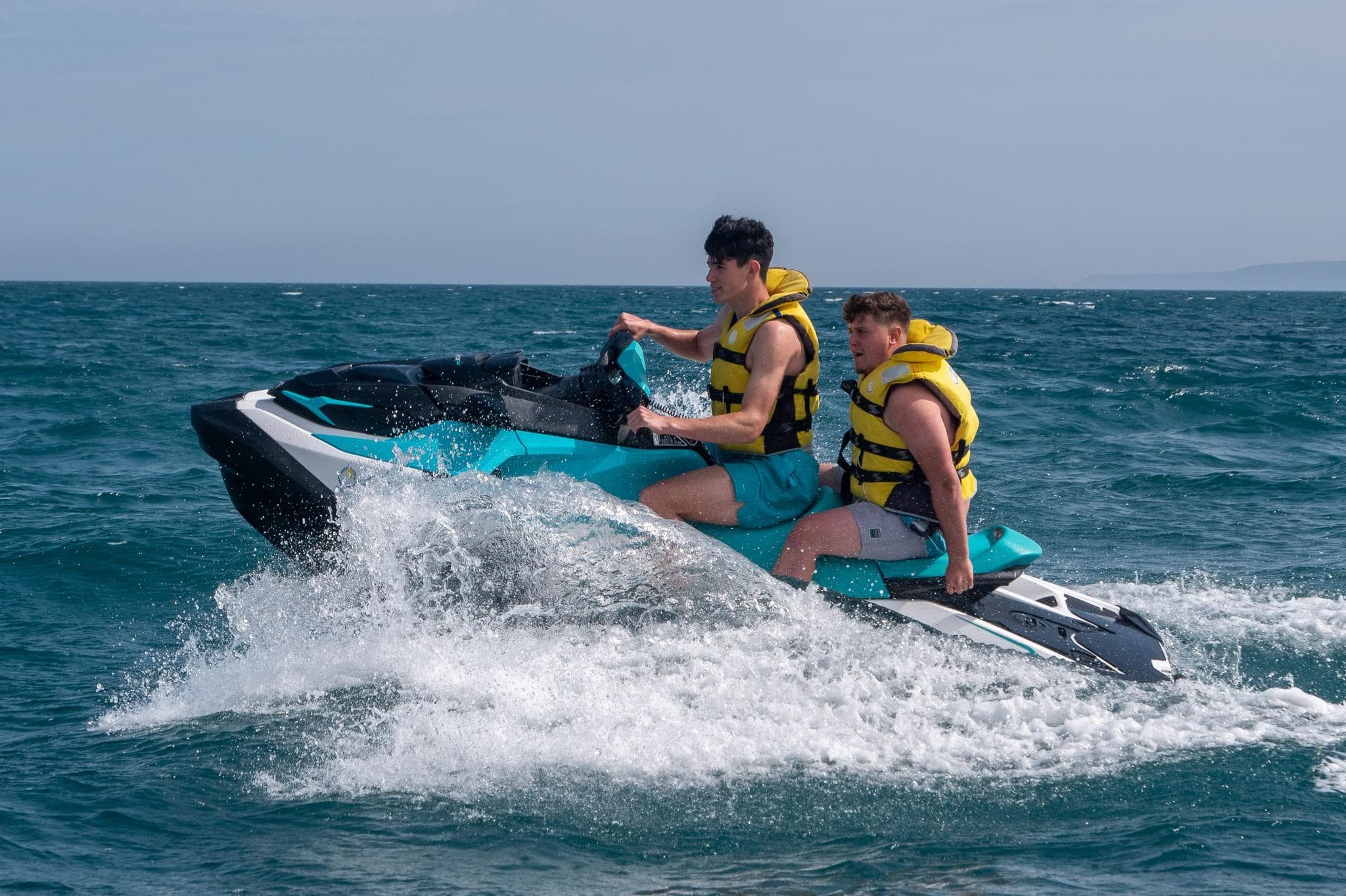 Two riders on a jet ski speeding across a lake with splashing waves