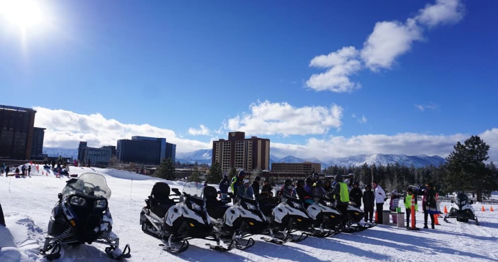 Snowmobile tour group parked near lodge with snowy mountain skyline