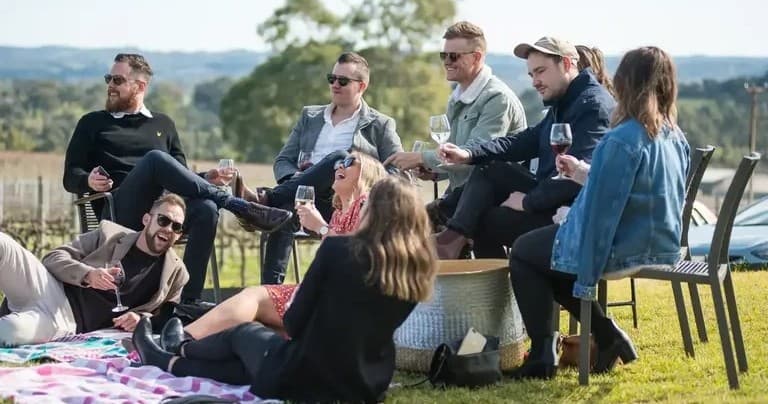 Group picnic and wine tasting on grassy vineyard lawn