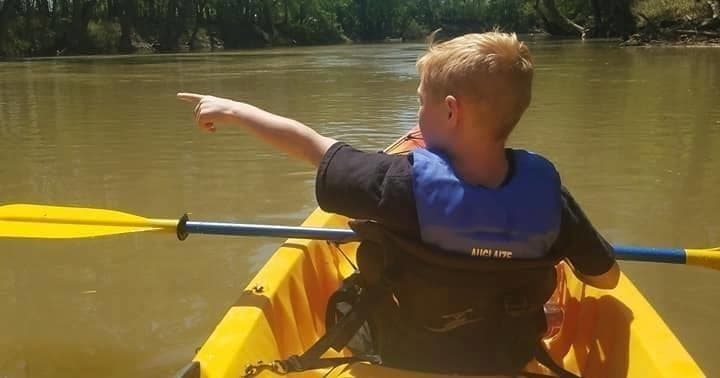 Child kayaking in bright yellow kayak on slow muddy river