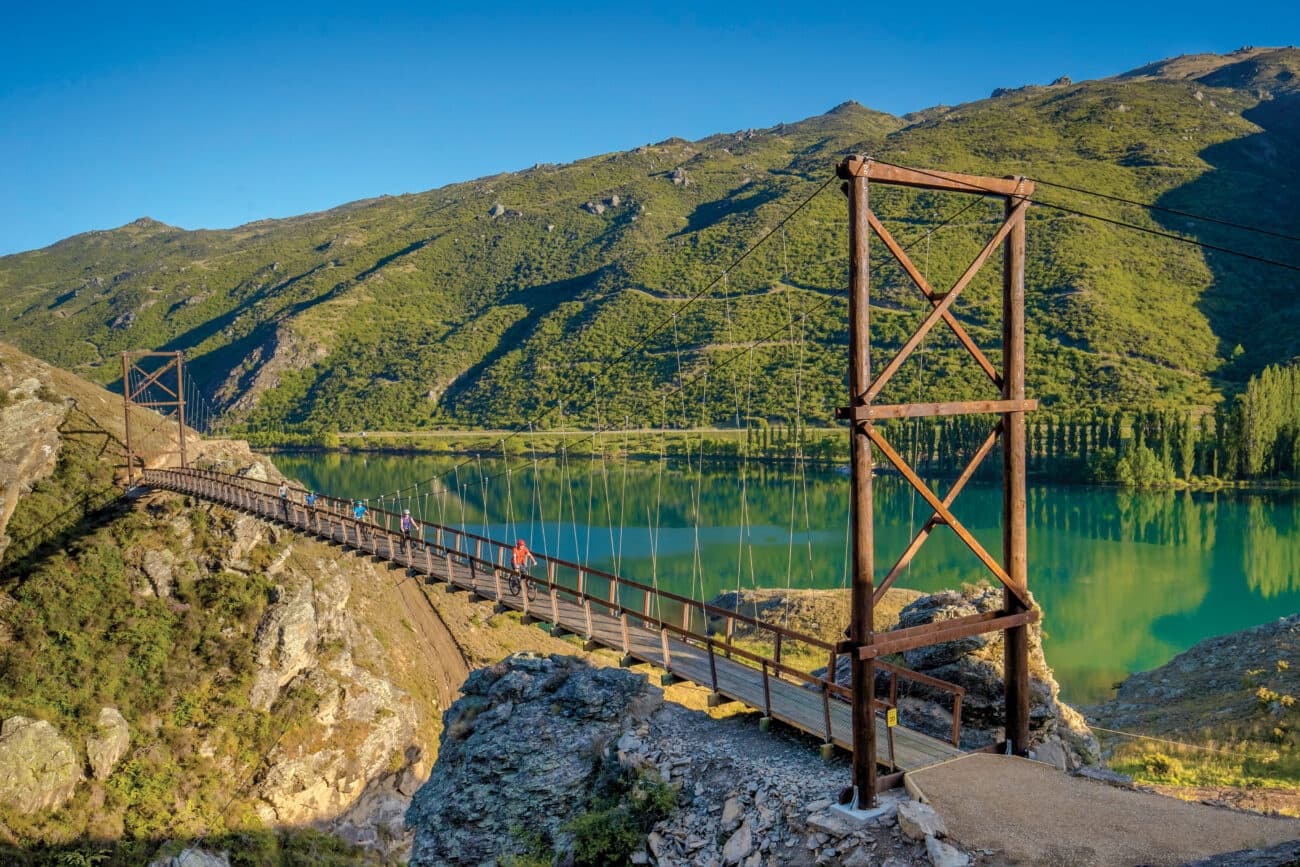 Hikers crossing suspension bridge over turquoise alpine lake