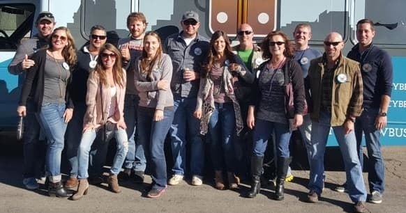 Group of brewery tour guests posing outdoors beside tour bus